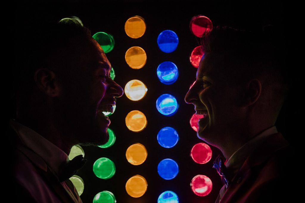 A couple is silhouetted against a backdrop of colorful circular lights, their profiles illuminated in a vibrant display of red, blue, green, and yellow hues