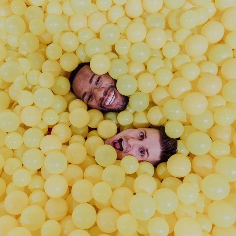 DeAndre and Stuart smiling in a yellow ball pit during a colorful LGBTQ engagement session