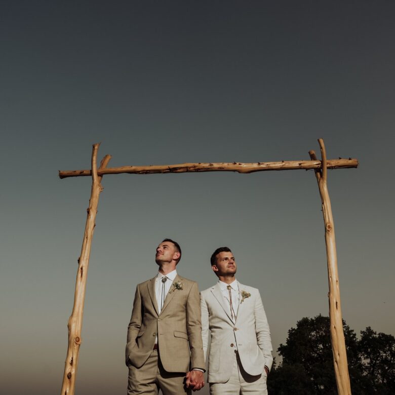 Patrick and Colby holding hands beneath a rustic ceremony arch at their private ranch wedding near Austin