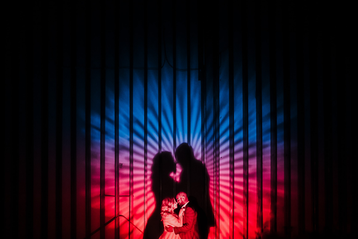 Creative silhouette of a bride and groom with vibrant blue and red lighting casting dramatic rays on a corrugated backdrop at Springdale Station in Austin, Texas