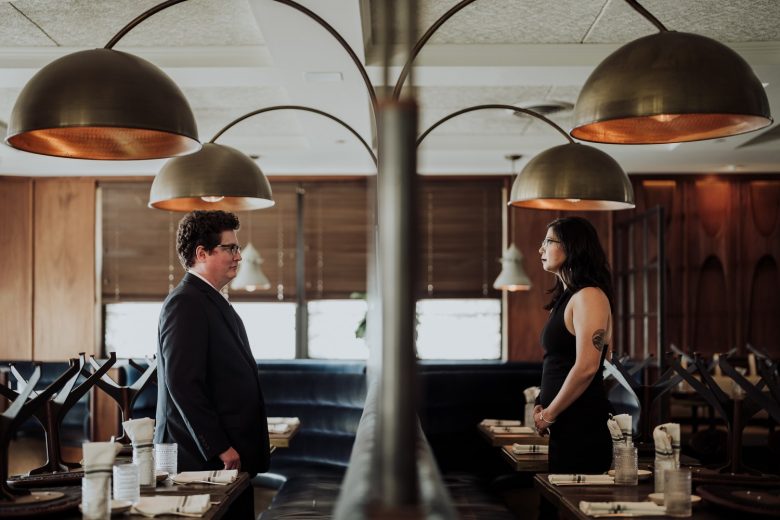 Elissa and Walt face each other beneath sculptural brass lamps inside Eberly in Austin.
