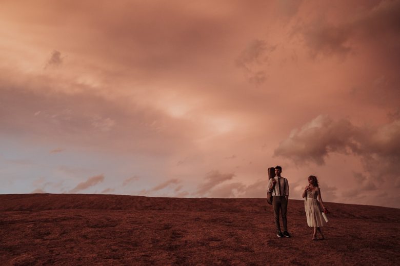 Couple walking across Enchanted Rock under a dramatic pink sunset sky